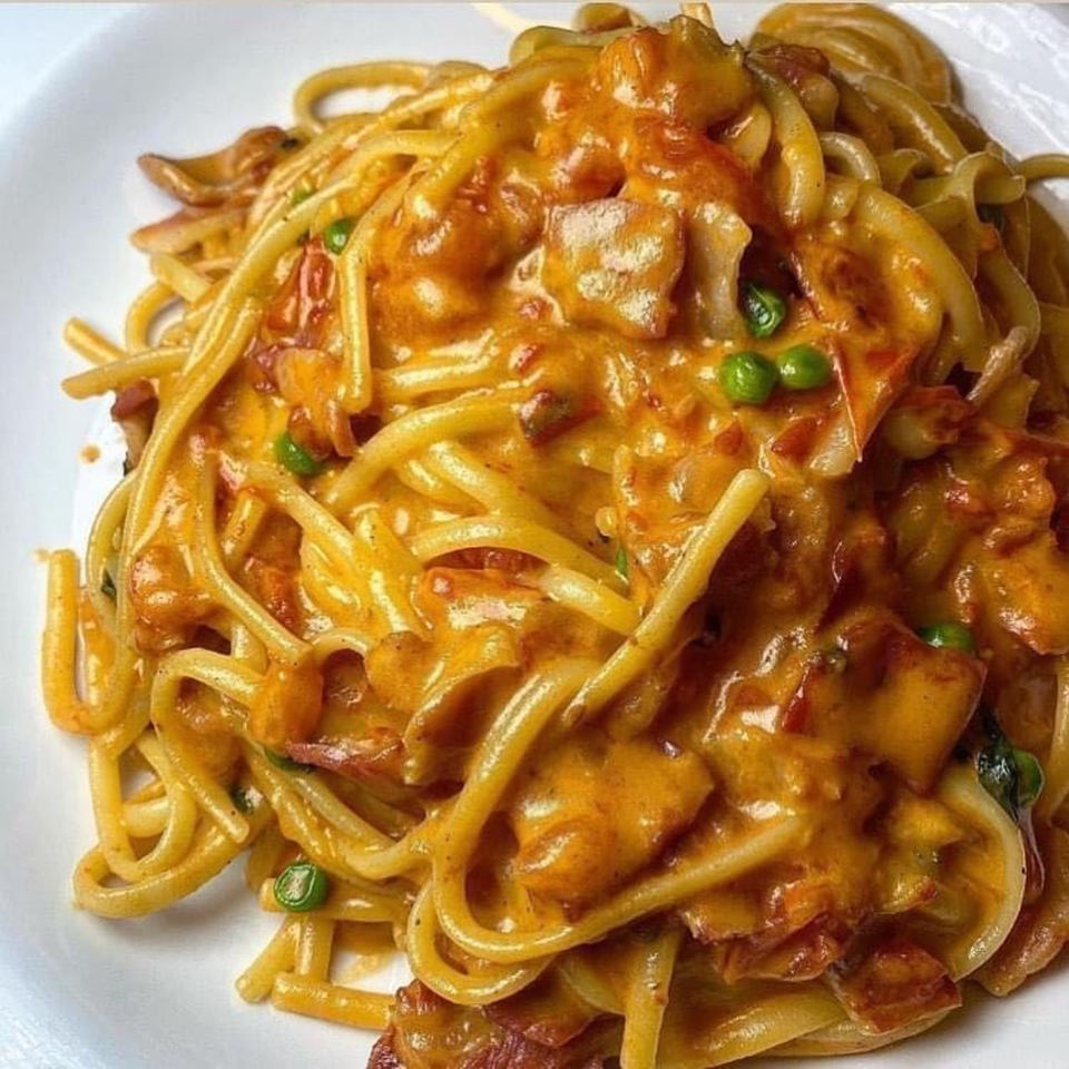 Close-up of Cafe Gia's spaghetti carbonara with peas and bacon in a creamy orange sauce.